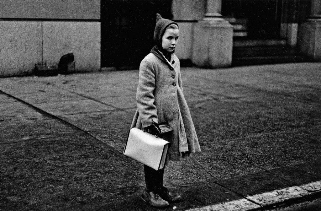 Girl with a pointy hood and white schoolbag at the curb, N.Y.C., 1957 by Diane Arbus